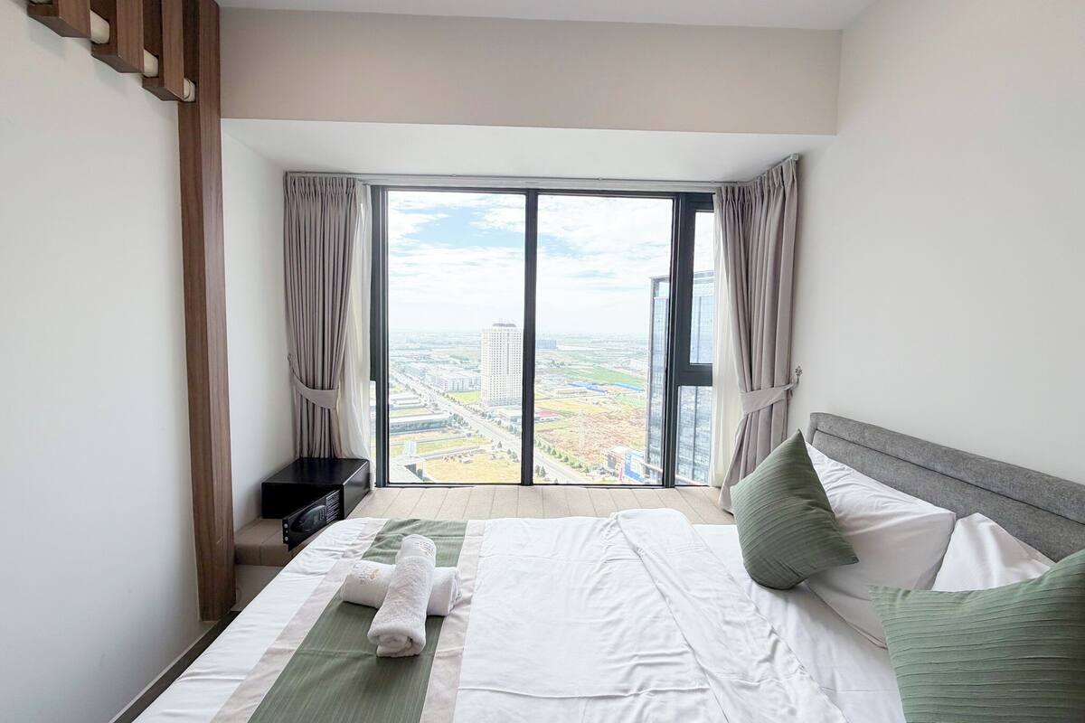 Habitación de hotel con una cama grande, vistas de la ciudad a través de ventanales del suelo al techo y una escalera moderna.