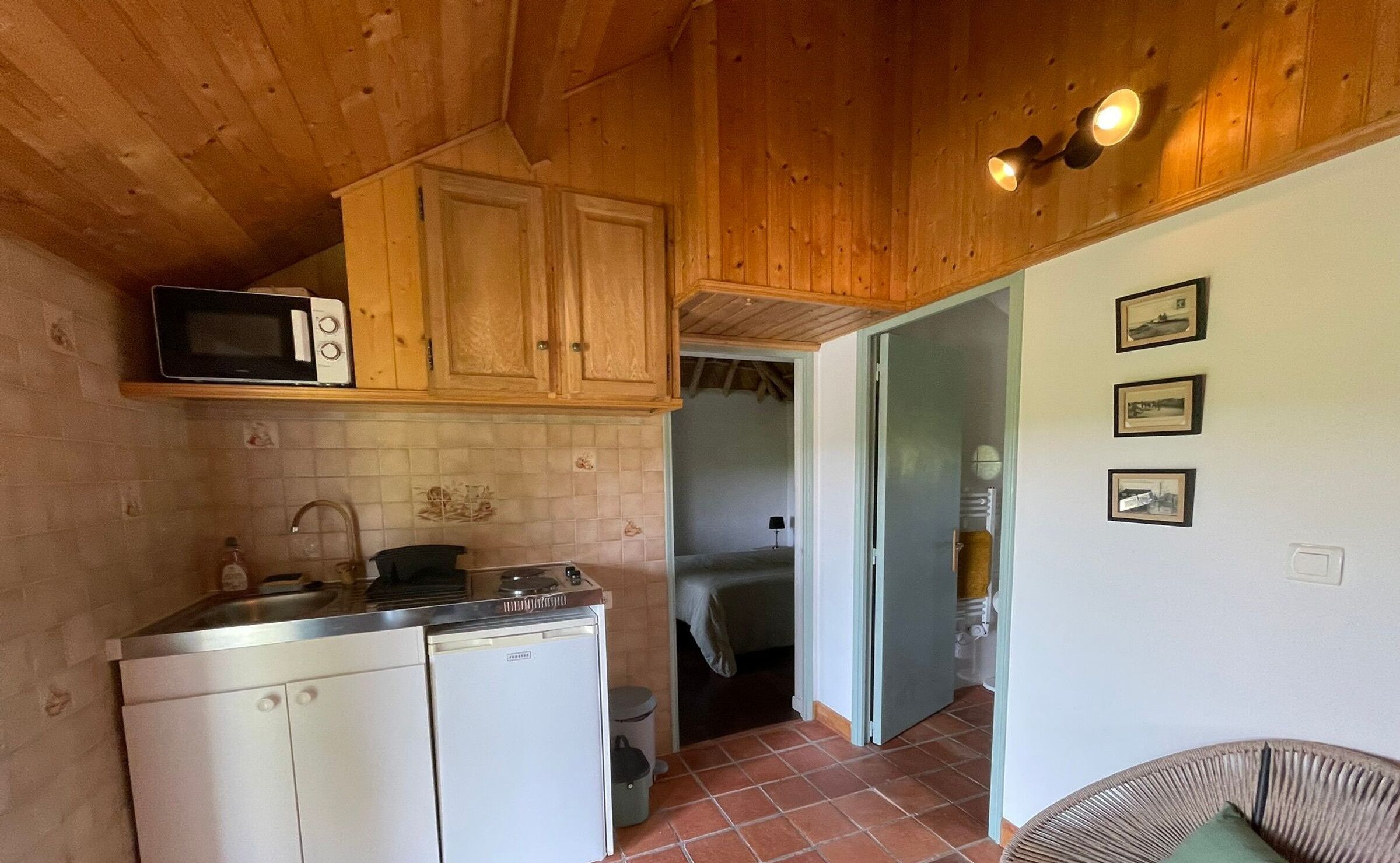 Eine kleine Küche mit Mikrowelle, Herd und Schränken. Ein Korbstuhl mit Kissen befindet sich im Vordergrund.