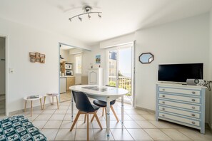 A room with a dining table, chairs, a TV, a dresser, and a view of the outside. - Cap Sur L’océan – Beautiful Sea View (Pornic)