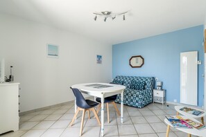 A room with a round table, two chairs, a sofa, a small bedside table, and a radiator. - Cap Sur L’océan – Beautiful Sea View (Pornic)