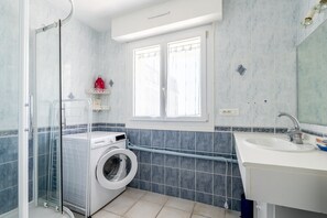 Une salle de bain équipée d’un lave-linge, d’un évier et d’une fenêtre.