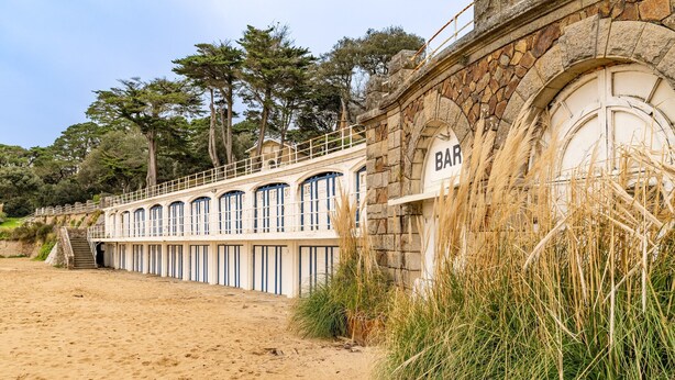 A seaside bar with a stone facade, a wooden deck, and a view of the beach.