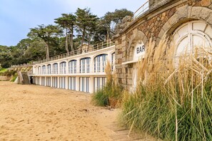 Un bar en bord de mer, avec une façade en pierre, une terrasse en bois et une vue sur la plage.