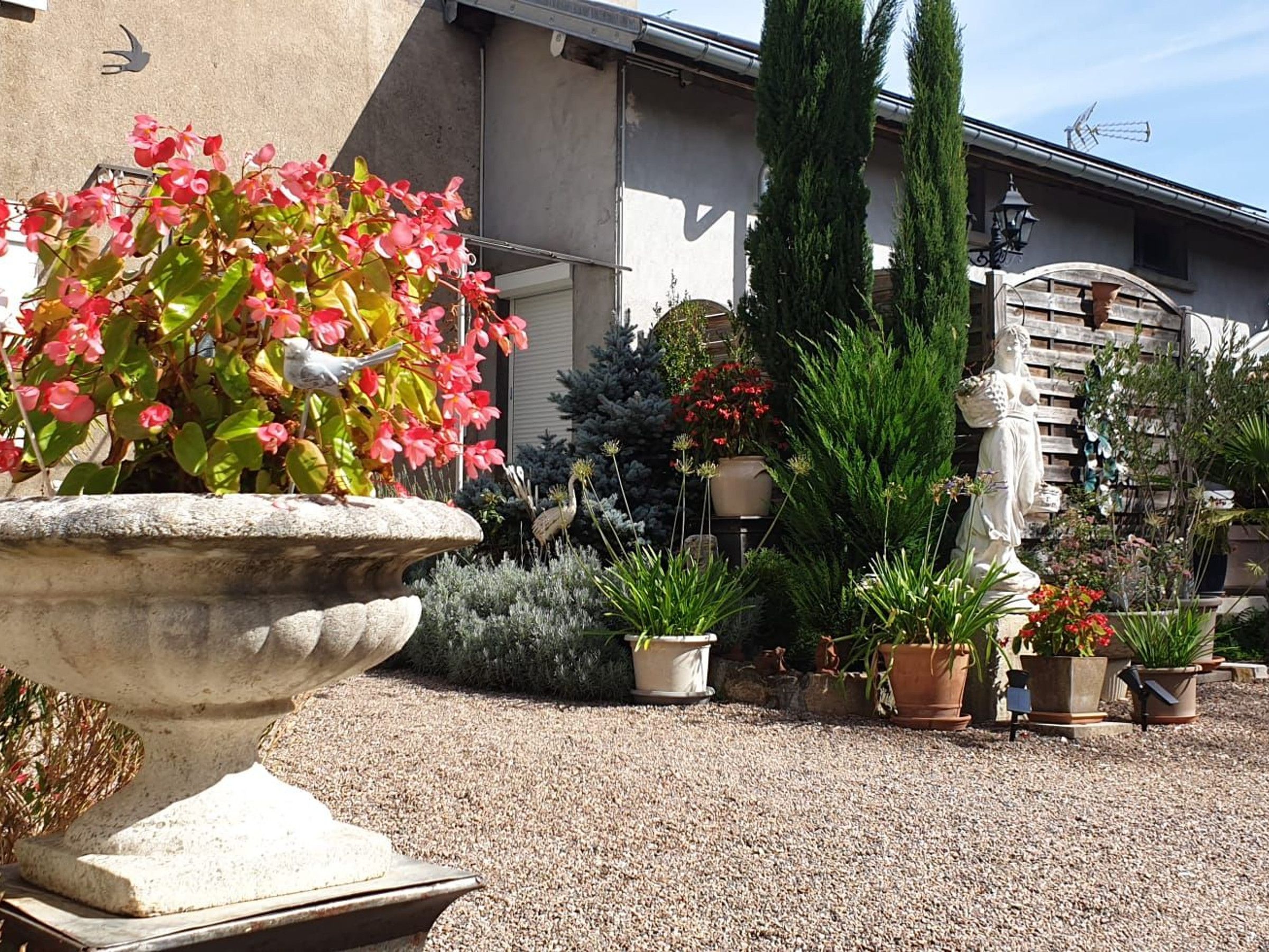 A garden with a variety of potted plants and a large stone planter with pink flowers.