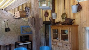 A rustic room with wooden walls, a wooden cabinet with glass doors, a television, and blue plastic chairs. - Charming Studio with Garden and Terraces, Peaceful and Historic Setting (Mersuay)