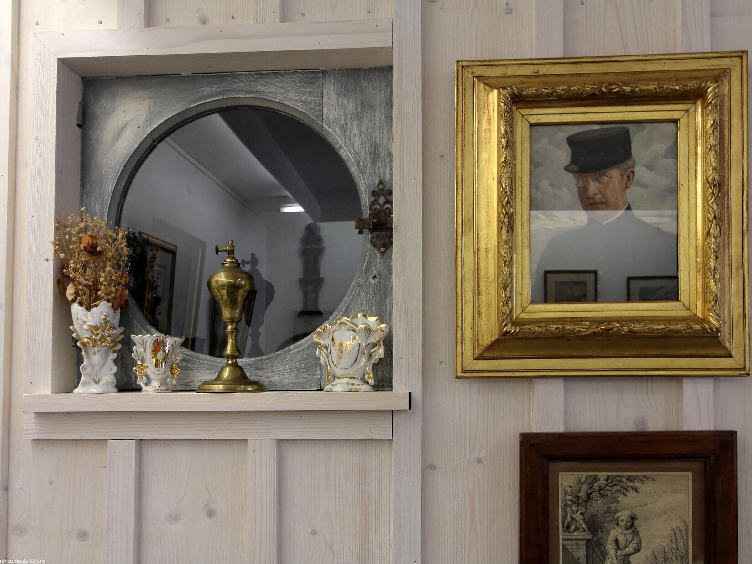 A mirror with a gold frame, a brass candelabra, and decorative vases on a wall.
