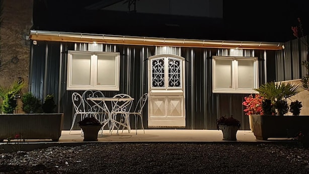 A covered outdoor seating area with a table and chairs, a decorative window, and potted plants. - Charming Studio with Garden and Terraces, Peaceful and Historic Setting (Mersuay)