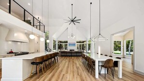 Une cuisine spacieuse dotée d’un îlot central, de planchers en bois et de luminaires suspendus modernes.