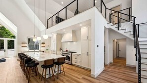Une cuisine moderne dotée d’un îlot central, de meubles blancs et d’un escalier noir.