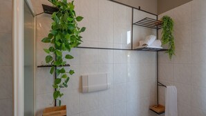 Et badeværelse med hvide fliser, et håndklædestativ, en hylde med en plante og en træbakke.