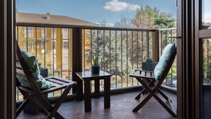 En balkon med to træstole og et lille bord, med udsigt over et boligområde med træer og bygninger.
