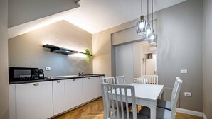 Eine moderne Küche mit weißen Schränken, einer schwarzen Arbeitsplatte und einem eingebauten Herd. Ein Esstisch mit weißen Stühlen und einer Pendelleuchte darüber.
