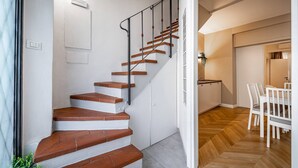 Eine Treppe mit weißen Wänden und Holzbodenstufen führt zu einer Küche mit Esstisch und Stühlen.