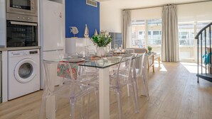 A modern kitchen with stainless steel appliances, a glass dining table with clear chairs, and a view of the city through large windows. - Charming triplex with jacuzzi in Calonge (Calonge)
