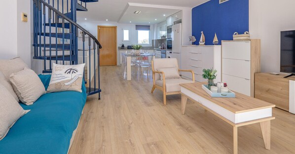 A modern living room with a blue sofa, wooden coffee table, and a staircase with blue railings.