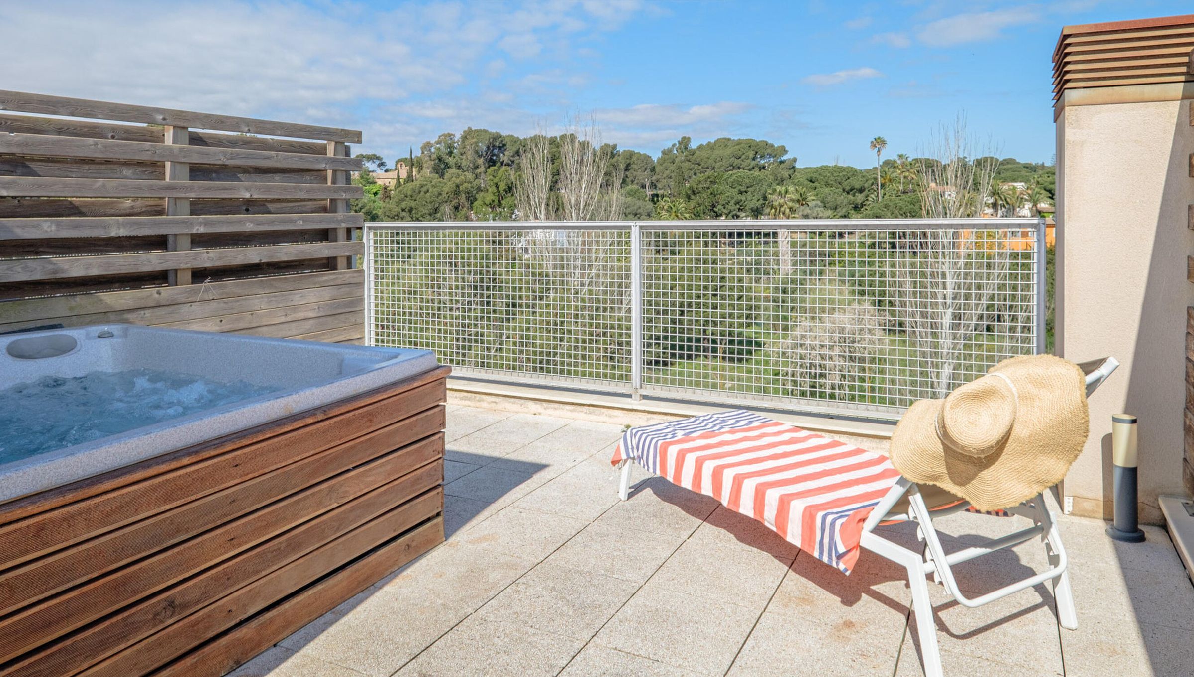 Une terrasse sur le toit avec un jacuzzi, une chaise longue à rayures et une clôture en bois.