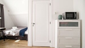 Een slaapkamer met een bed, een witte kledingkast, een magnetron en een deur.