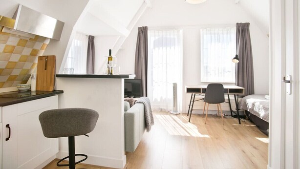 Een compact appartement in moderne stijl, met een kitchenette, een eethoek en een slaapkamer.