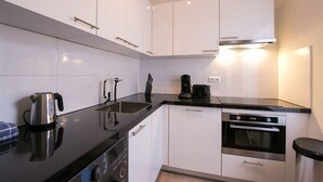 A modern kitchen with white cabinets, a black countertop, a kettle, a coffee maker, and an oven. - Modern apartment near Scheveningen beach (Den Haag)