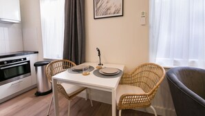 A modern kitchen with white cabinets, a stainless steel oven, and a dining area with a white table and wicker chairs. - Modern apartment near Scheveningen beach (Den Haag)