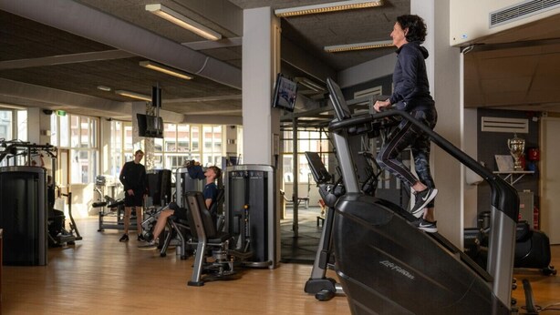 Een sportschool met loopbanden, gewichtstoestellen en een grote spiegel.