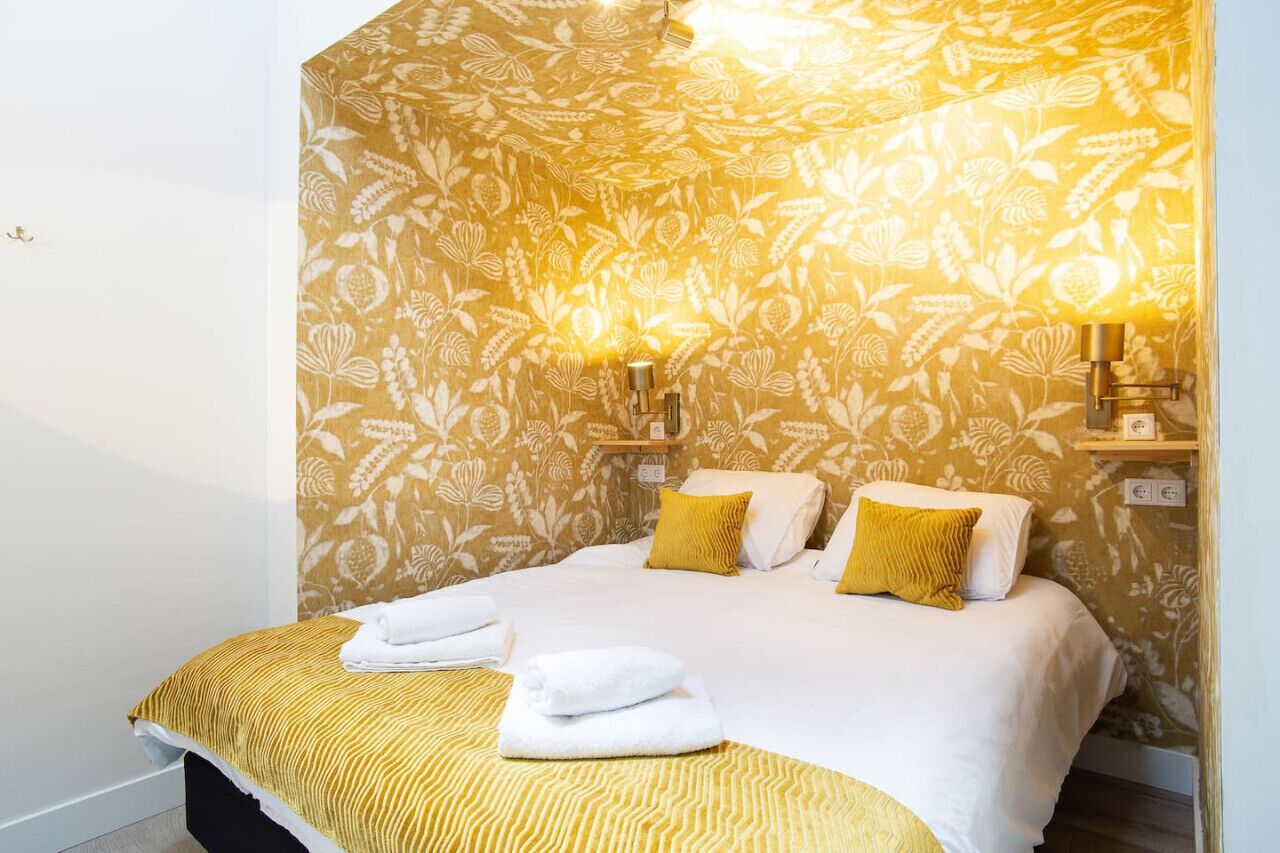 A hotel room with a bed, two wall-mounted lamps, and a patterned wallpaper.