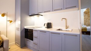 Een compacte keuken met grijze kastjes, een zwarte oven, een spoelbak en een koffiezetapparaat.