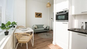A modern kitchen with white cabinets, a built-in oven, and a dining area with a table, chairs, and a floor lamp. - Modern apartment near Scheveningen beach (Den Haag)