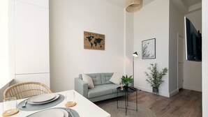 A modern living room with a grey sofa, a dining table set with plates and glasses, a world map artwork, a lamp, and a potted plant. - Modern apartment near Scheveningen beach (Den Haag)