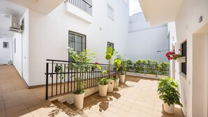 Un amplio patio con plantas en macetas y suelo de baldosas, rodeado de paredes blancas y balcones.