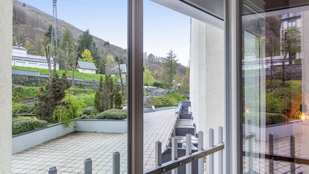 A balcony with a view of a landscaped area, including trees and a building in the background.