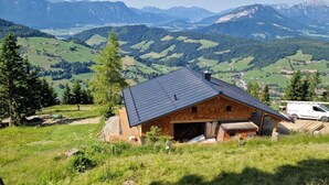 A rustic mountain cabin with a sloped roof, surrounded by lush green fields and distant mountains. - Panoramic hut in the ski area (Wildschönau-Niederau)
