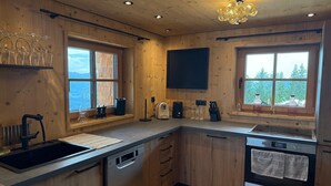 A modern kitchen with wooden cabinets, a large window, and a built-in oven. - Panoramic hut in the ski area (Wildschönau-Niederau)