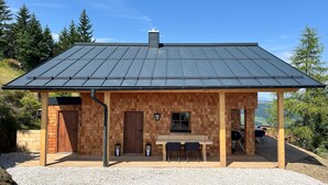 A wooden cabin with a metal roof, a wooden deck, and a view of the surrounding forest. - Panoramic hut in the ski area (Wildschönau-Niederau)