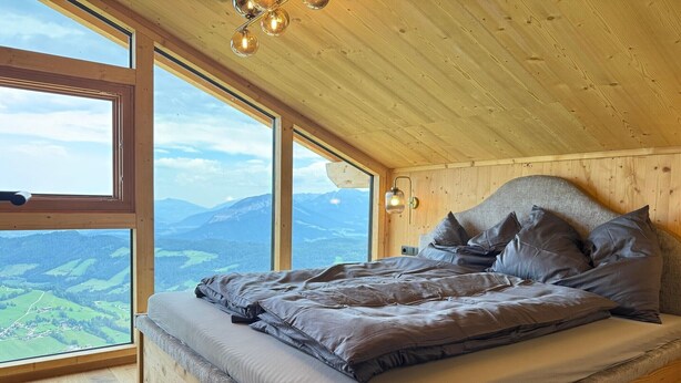 A bedroom with a large window, wooden ceiling, and a bed with pillows. - Panoramic hut in the ski area (Wildschönau-Niederau)
