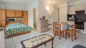 A compact hotel room with a bed, a small dining table with chairs, a kitchenette, and a bathroom.