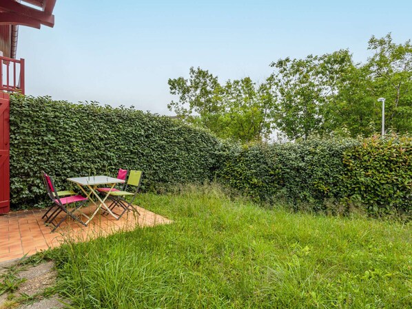 Un espacio al aire libre con una mesa y sillas, una estructura roja y un muro de setos.