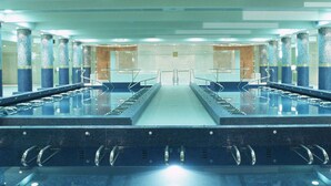 A large indoor swimming pool with multiple lanes, surrounded by columns and a tiled floor.