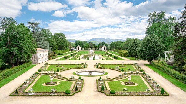 A formal garden with symmetrical pathways, a central fountain, and classical architecture.