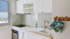A kitchen with white cabinets, a black stove, a white sink, and a window with a view of the outdoors. - Ground floor apartment near sea, sleeps 4 (Bernières-sur-Mer)