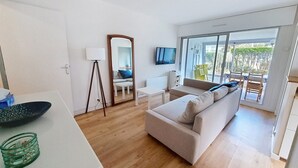 A modern living room with a sofa, a TV, and a large window offering a view of the outdoors. - Ground floor apartment near sea, sleeps 4 (Bernières-sur-Mer)