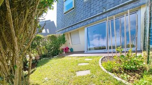 A modern house with a well-maintained garden, a paved pathway, and a large sliding glass door. - Ground floor apartment near sea, sleeps 4 (Bernières-sur-Mer)