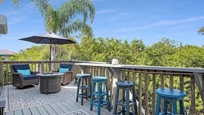 A deck with outdoor furniture, including a table and chairs, and a large umbrella. - Spacious 3BR, 2BA beach home just a short walk from the sand! Three bedrooms up, private queen room and bath down. Secure 2-car garage for vehicles or a small boat. Perfect for families or groups. 30-day minimum stay required. (New Smyrna Beach)
