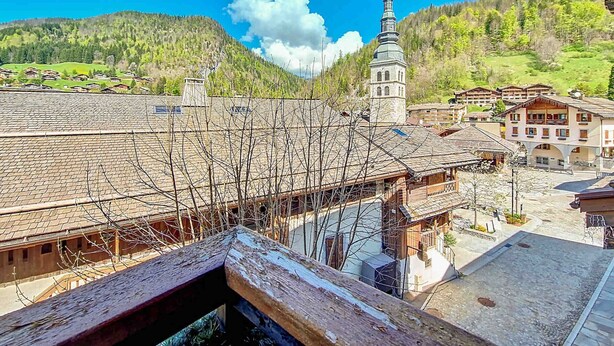 A traditional chalet-style building with a sloped roof, a bell tower, and a view of a mountainous landscape. - La Clusaz - Apartment 6 ppl, 53 sqm, 2 bedrooms, WiFi (La Clusaz)
