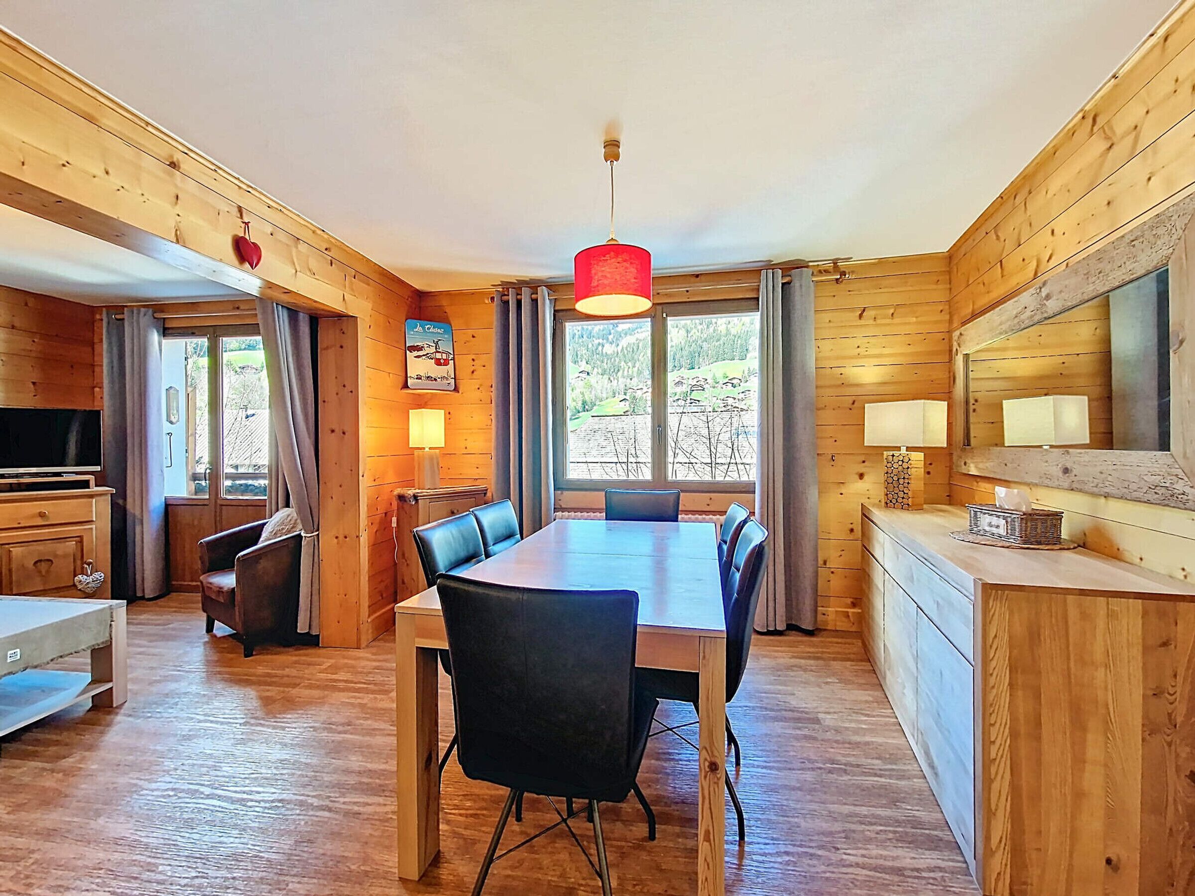 A wooden cabin with a dining area, a TV, and a large window with a view of the outdoors.