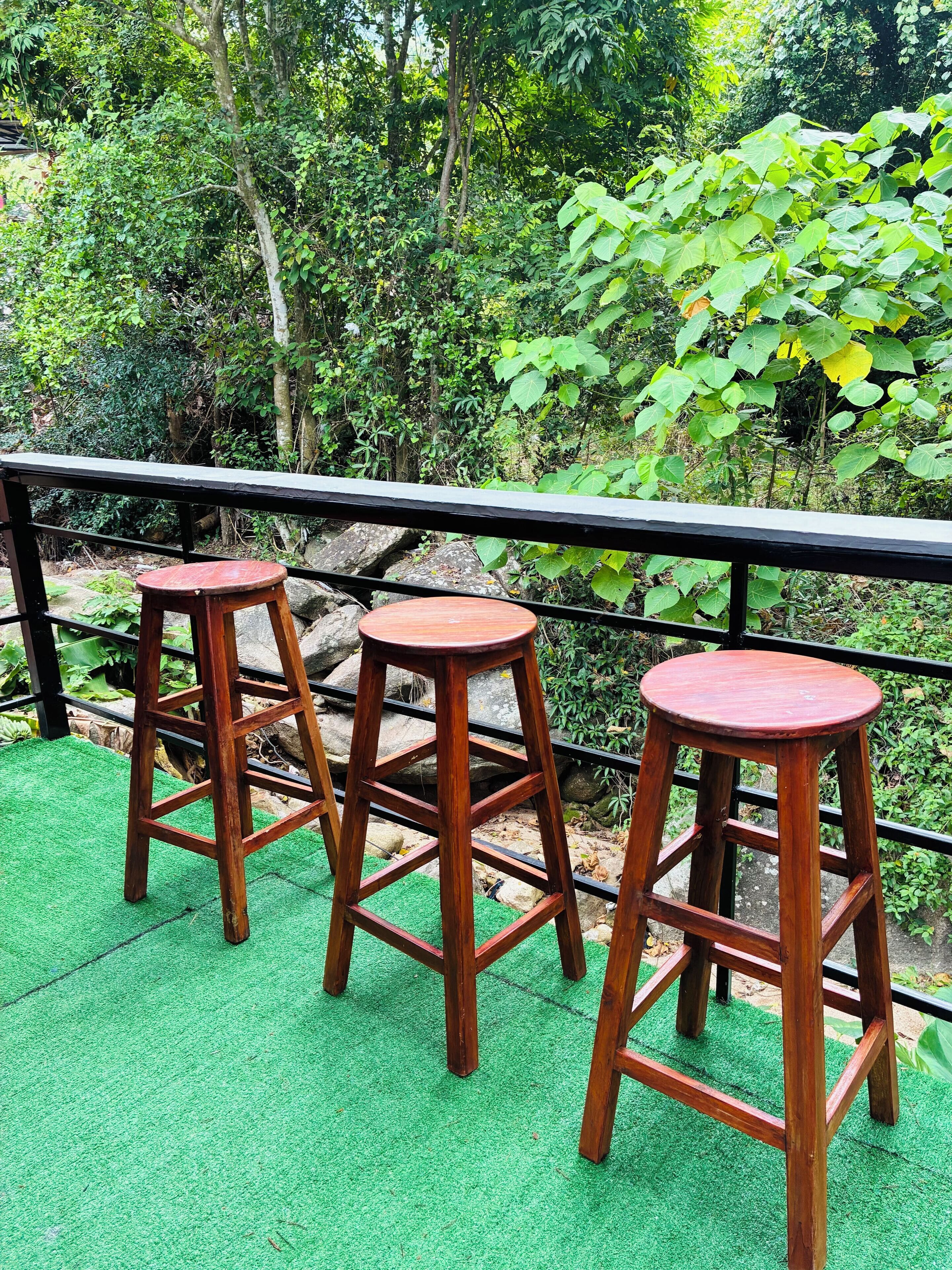 Three wooden stools on a green surface with a black metal railing in the background.