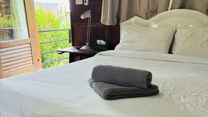 Een net opgemaakt bed met witte lakens en een opgevouwen grijze handdoek ernaast.