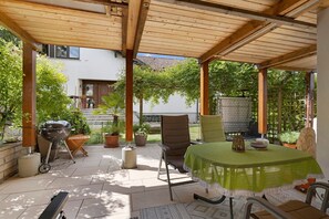 A covered patio with a table, chairs, a grill, and potted plants.