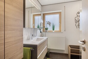 A modern bathroom with a wooden vanity, a large mirror, a window with plants, and a radiator.