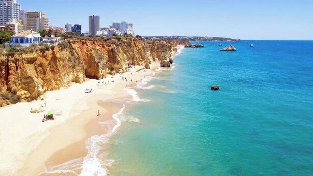 A coastal beach with a rocky cliff, clear blue water, and a city skyline in the background. - Charming 1-bedroom apartment in Portimão (Portimão)